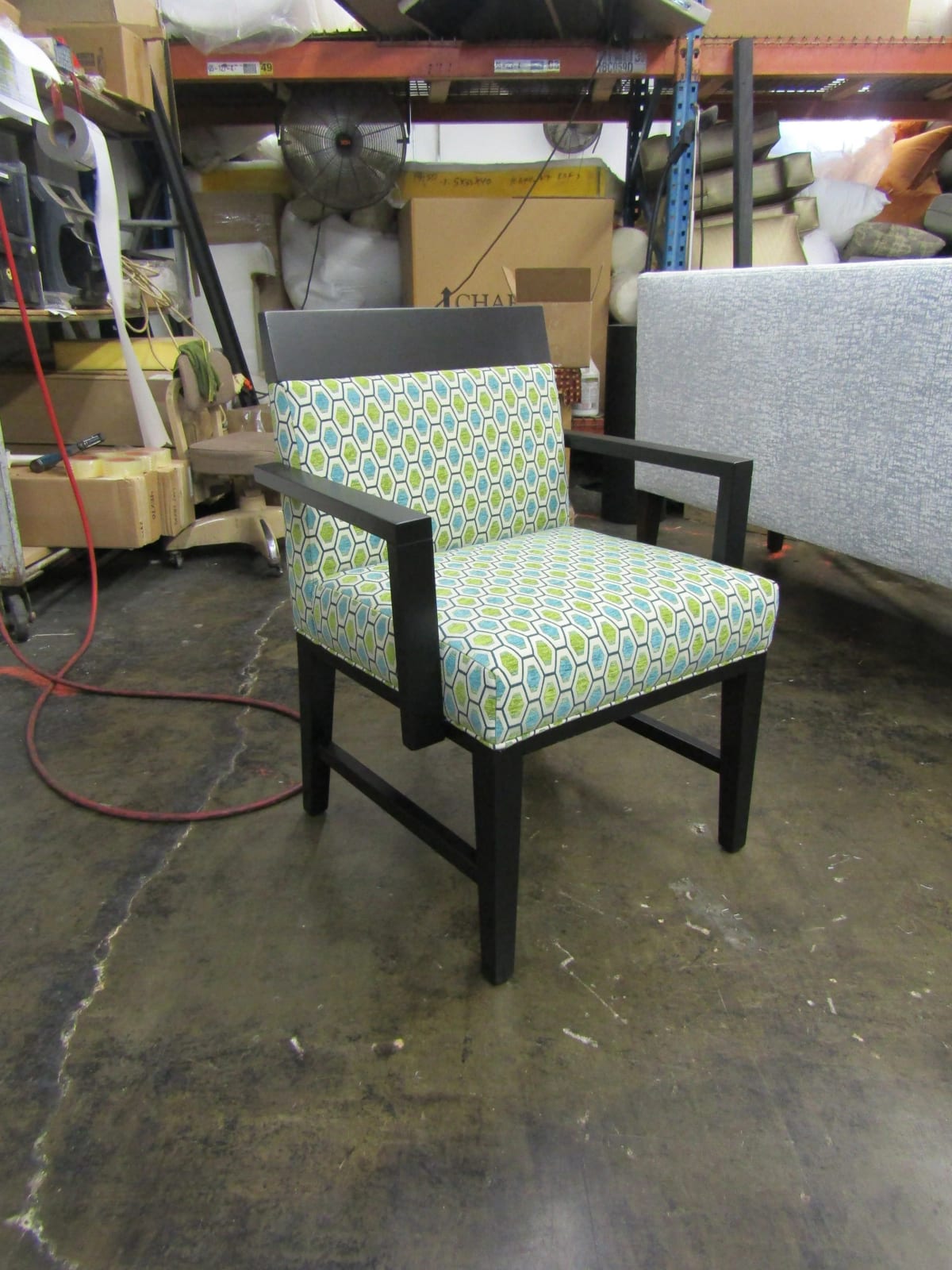 An accent chair in a green and white patterned fabric on a dark wood frame