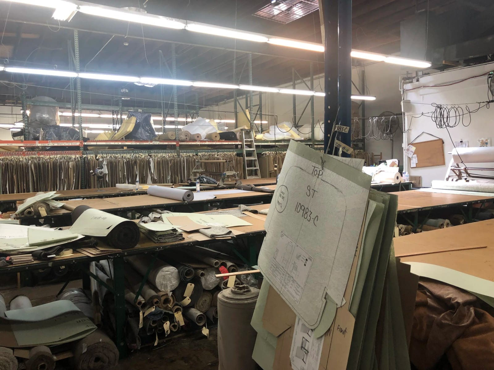 The cutting room: long tables, rolls of leather and fabric, and paper patterns hanging from a rail