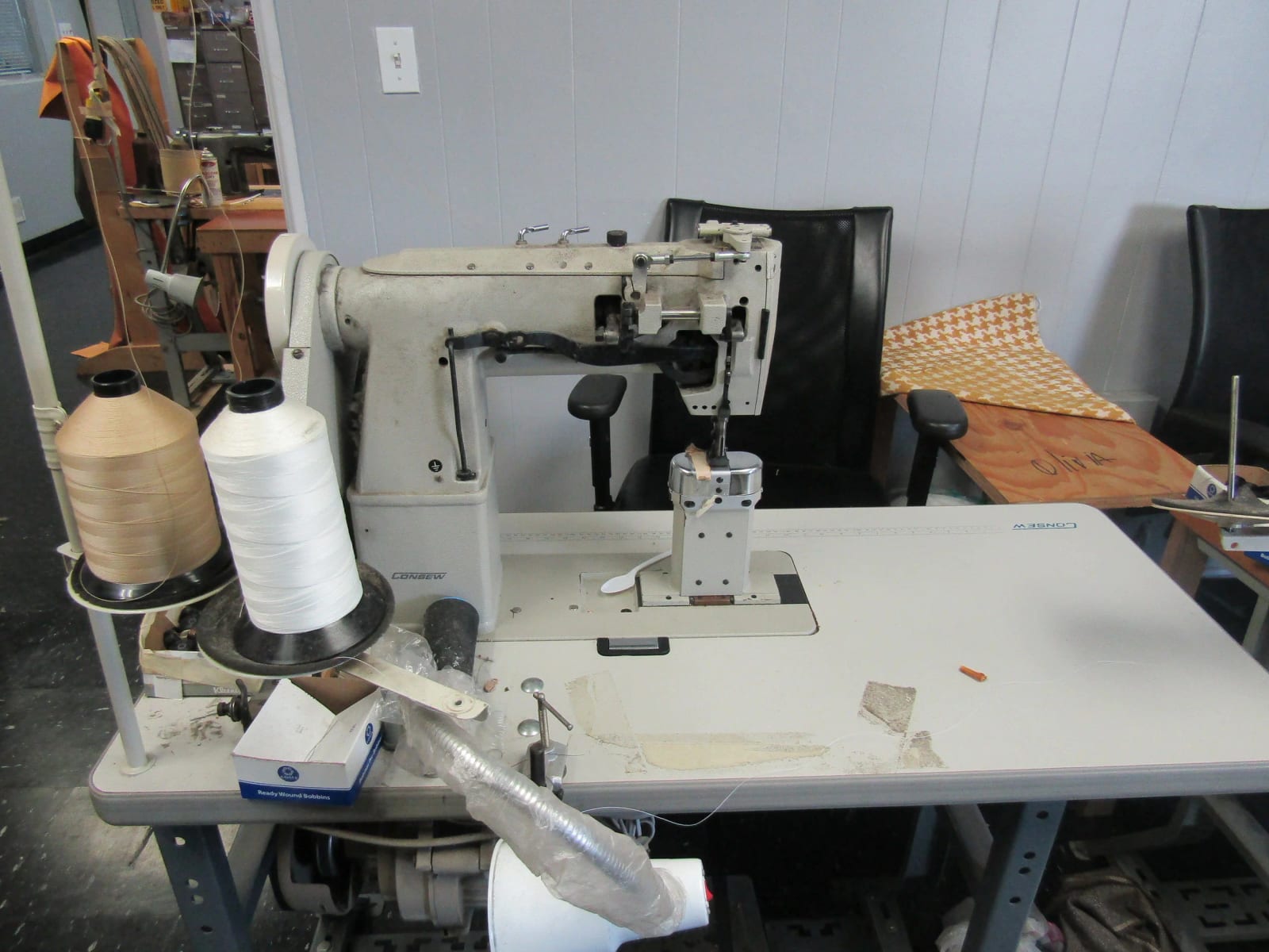 An industrial sewing machine with cones of thread beside it