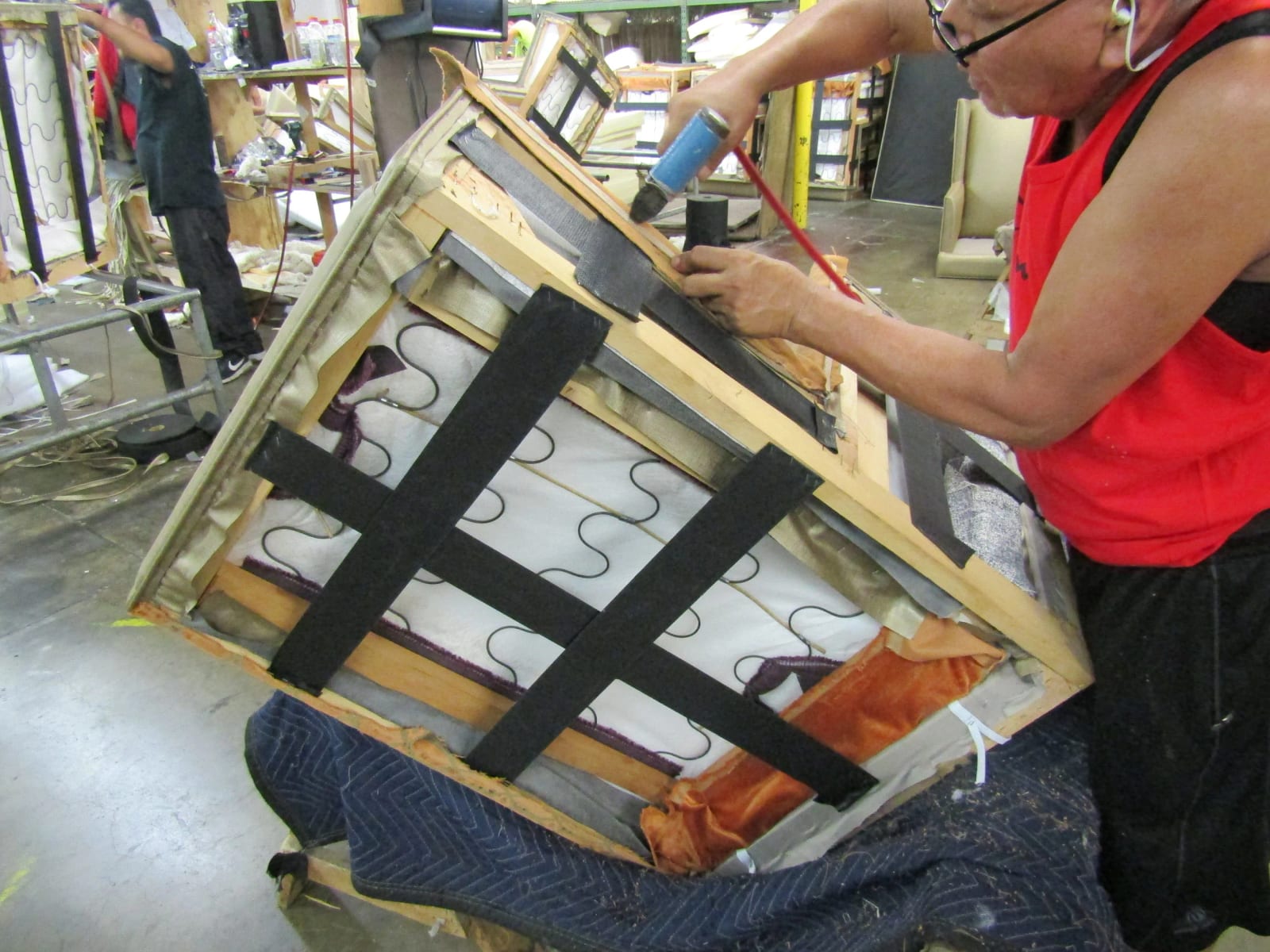 An upholsterer stapling black webbing across the springs under a seat frame