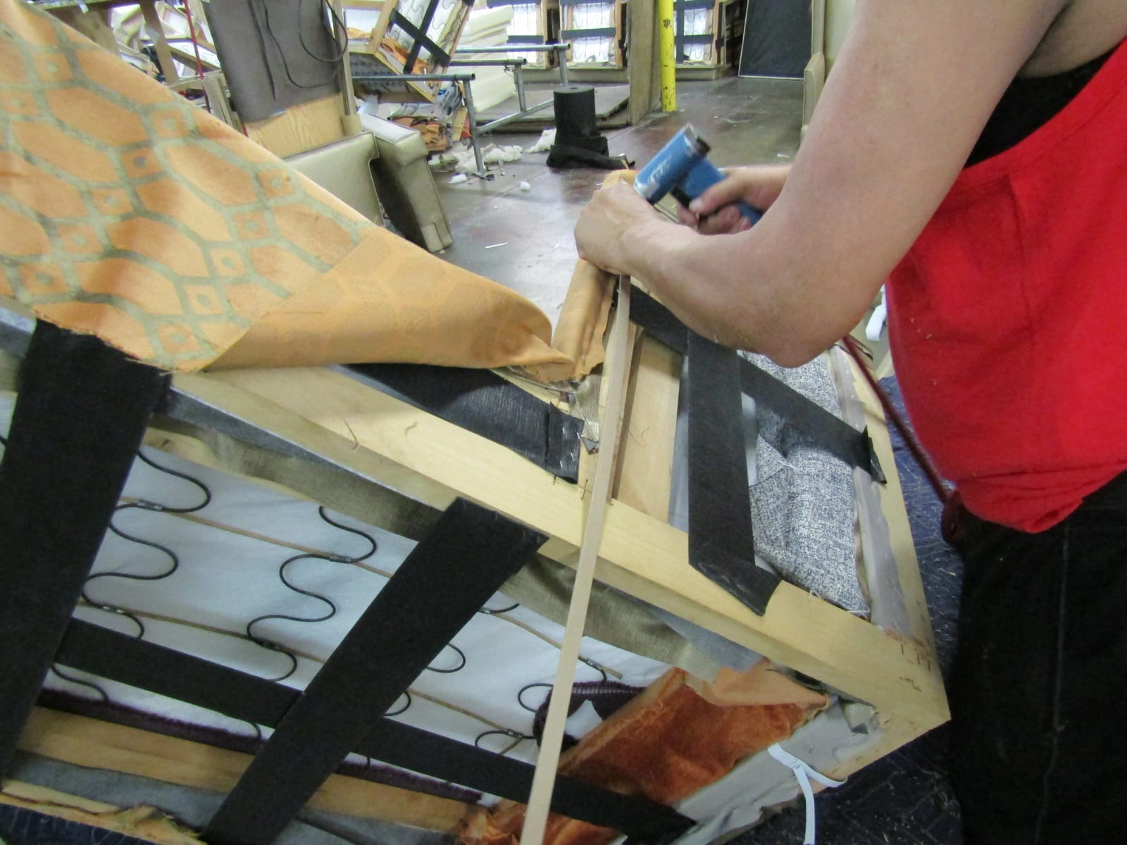 Hands stapling patterned fabric to a frame, with its springs and webbing showing